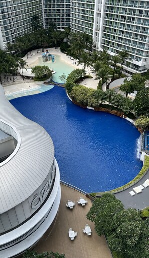 A large indoor pool with a curved design, surrounded by palm trees and a sandy area. - The Bawhaus (Parañaque)