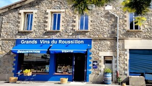 Un bâtiment en pierre avec une devanture bleue portant l’inscription « Grands Vins du Roussillon » et un auvent bleu indiquant les sections « Dégustation » et « Vente ».