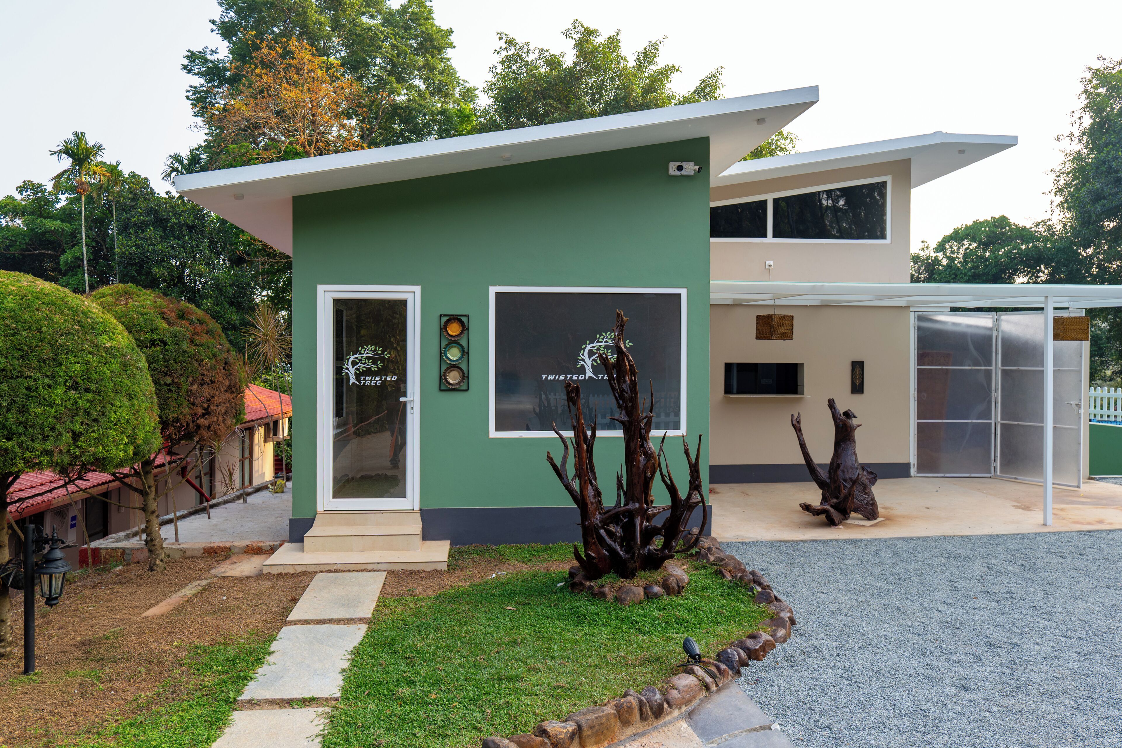 A modern building with a green facade, a glass door entrance, and a small garden area with a sculpture.