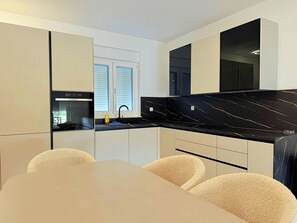 A modern kitchen with a black marble countertop, white cabinets, and a dining area with a beige table and chairs. - Apartment Top 2
with garden and swimming pool (Novalja)