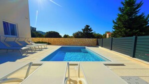 Ein Swimmingpool mit Liegestühlen, einer Steinmauer und einem Zaun.