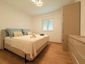 A bedroom with a bed, pillows, a bedside table, a window, and a wardrobe. - Apartment Top 2
with garden and swimming pool (Novalja)