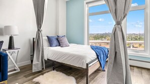 Ein Schlafzimmer mit Bett, Nachttisch, Lampe und Blick ins Freie.