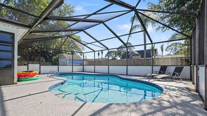A covered backyard with a swimming pool, lounge chairs, and a wooden fence.