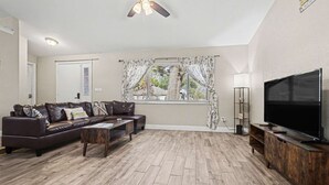 A living room with a sofa, coffee table, TV stand, and a ceiling fan.