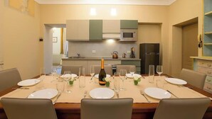 A dining area with a table set for six, a bottle of champagne, and a kitchen in the background.