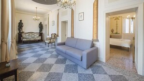 A room with a checkered floor, a sofa, a chair, a table, and a chandelier.