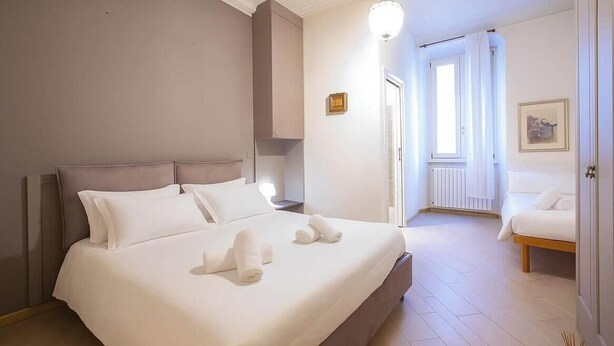 A hotel room with a bed, bedside tables, a nightstand, a window, and a door.