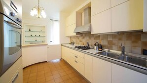 Una cocina moderna con armarios blancos, horno empotrado, estufa a gas y un lavamanos de acero inoxidable.