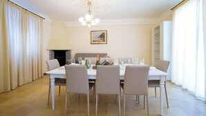 Un comedor con una mesa dispuesta para cuatro personas, una araña, una chimenea y un cuadro en la pared.