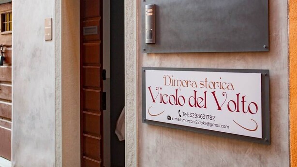 Fachada de edificio con puerta, cartel con datos de contacto y placa metálica con un número.
