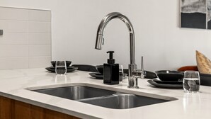 A modern kitchen with two stainless steel sinks, a black soap dispenser, and a glass of water on the counter. - Lux Downtown Urban Escape W/ Gym & 2 Free Parking (Calgary)