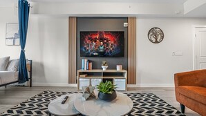 A modern living room with a flat-screen TV, a sofa, a coffee table, and a patterned rug.