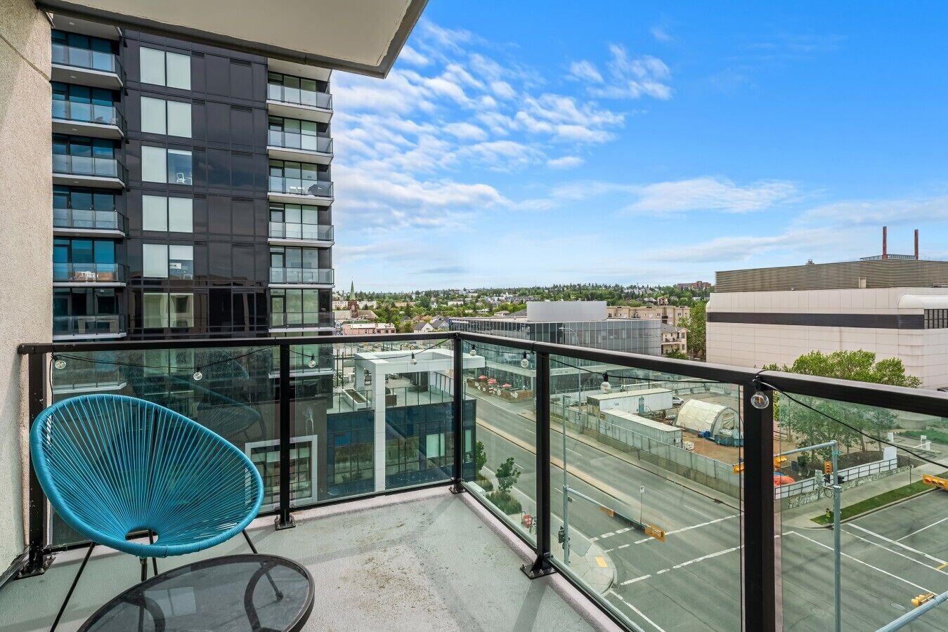 A balcony with a glass railing, a blue chair, and a view of a cityscape.