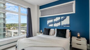 A modern hotel room with a large bed, a view of the city, and a blue accent wall.