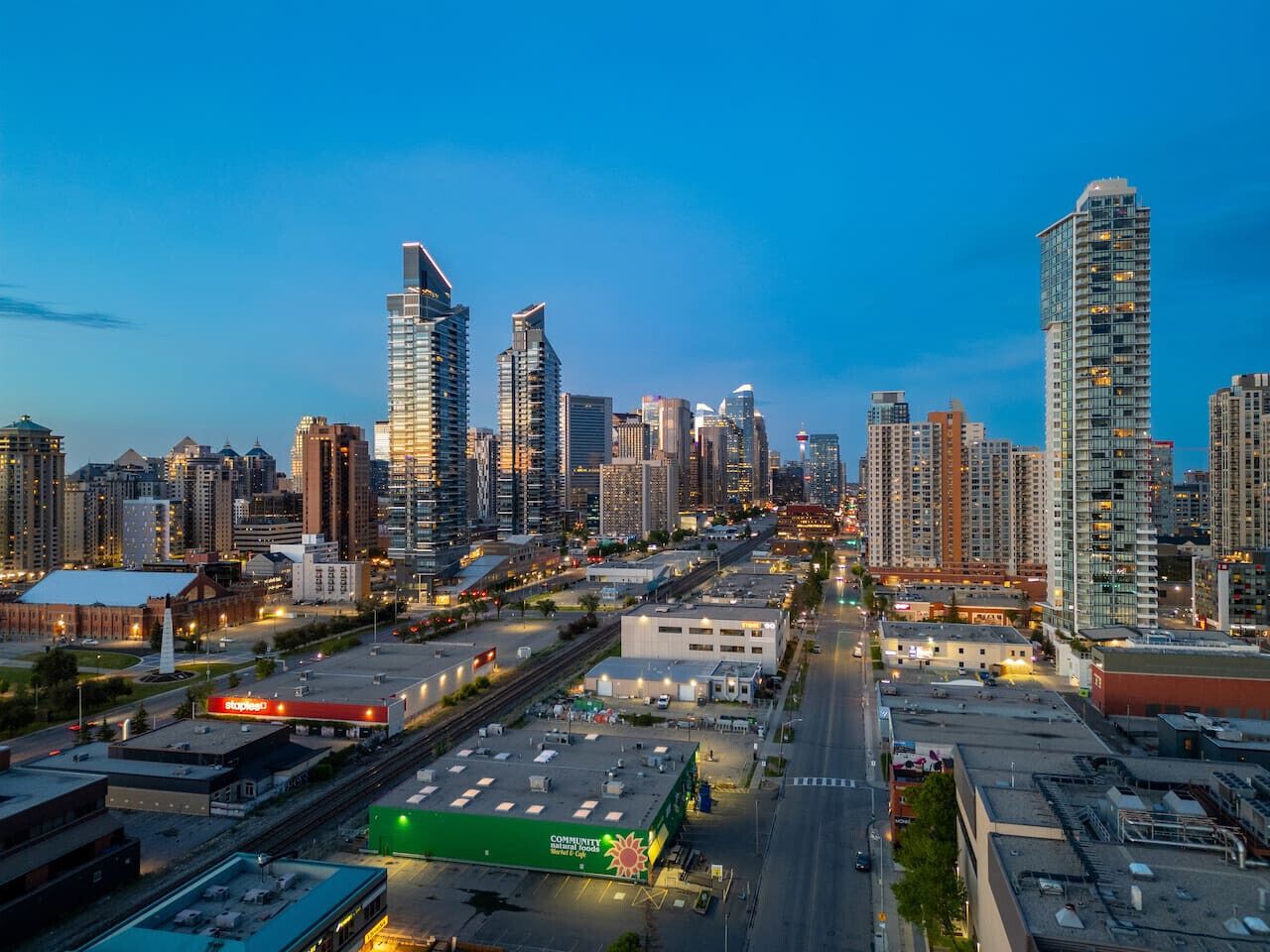 A cityscape with high-rise buildings, a wide road, and a green area with a sign.