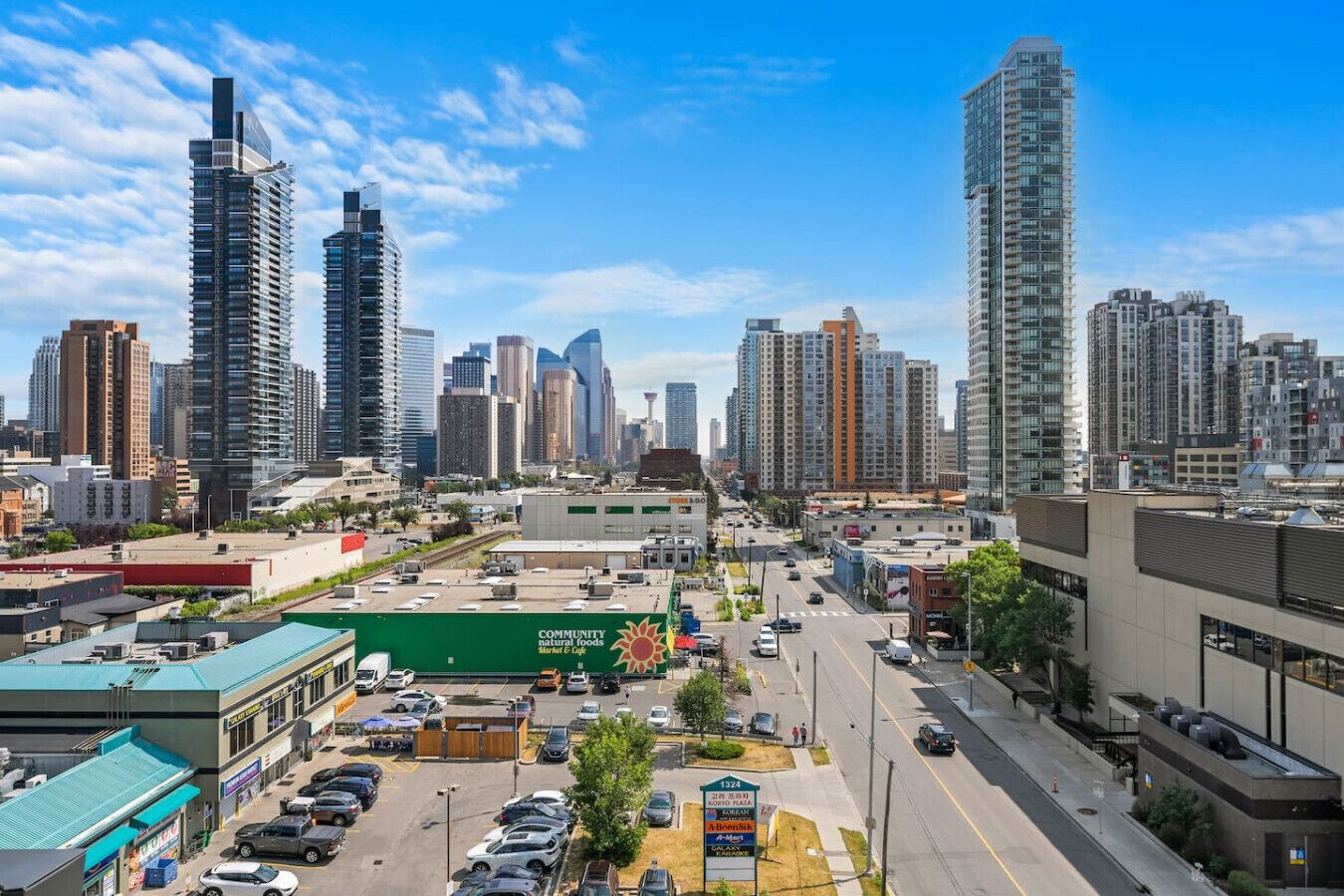 A cityscape with high-rise buildings, a parking lot, and a green building with a sign.