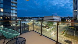 A balcony with a view of a cityscape at dusk, a chair, and a glass railing.