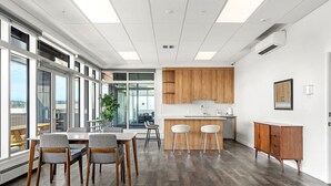 A modern kitchen with wooden cabinets, a dining area with a table and chairs, and large windows offering a view.