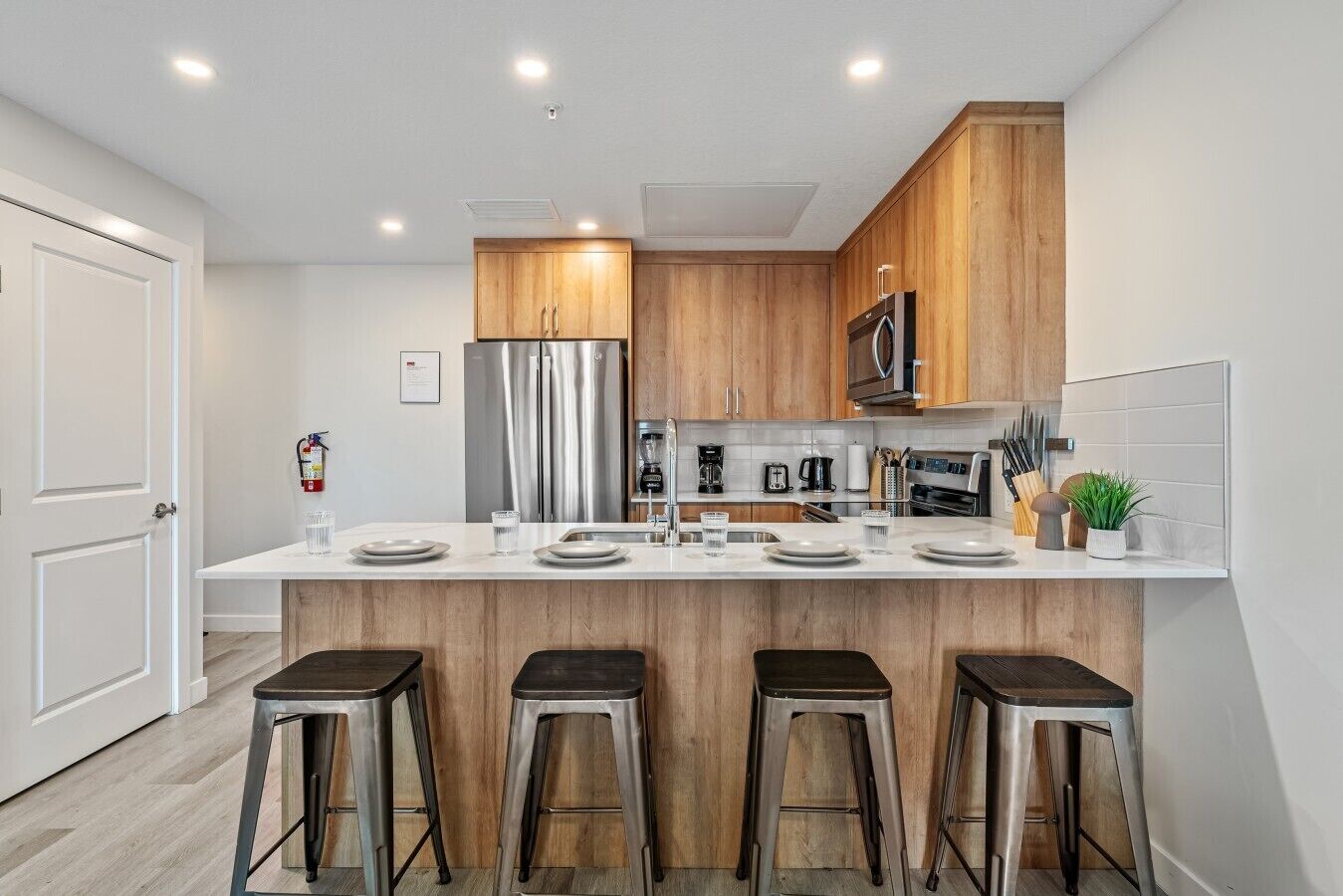 A modern kitchen with a central island, stainless steel appliances, wooden cabinets, and bar stools.