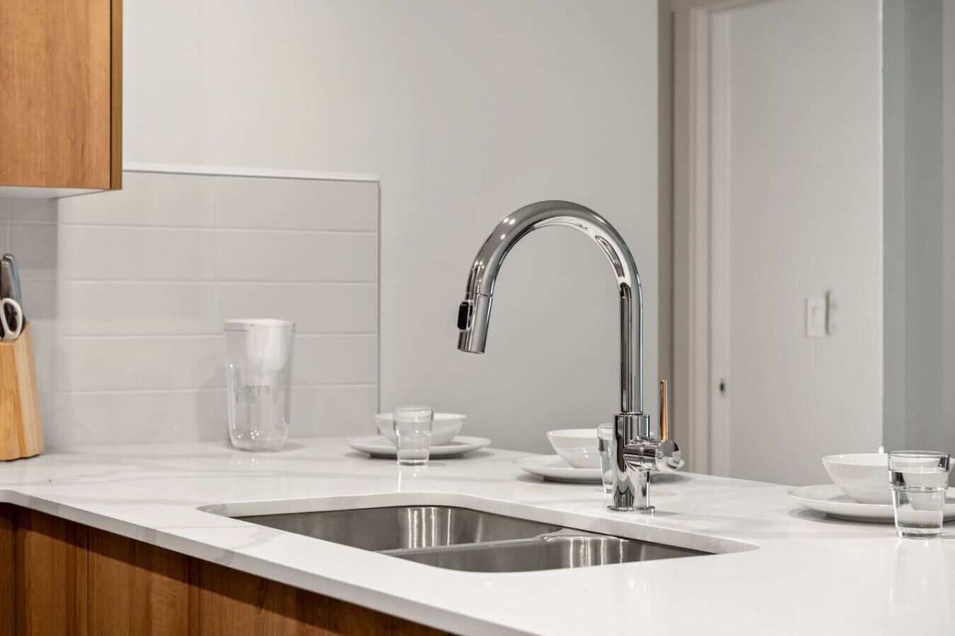 A modern kitchen with a stainless steel sink, a wooden cabinet, and a white tiled backsplash.