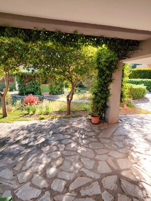 Eine terrasse mit Steinpflasterung, einer mit Grünwerk überwucherten Pergola, Topfpflanzen und einem gepflegten Garten.