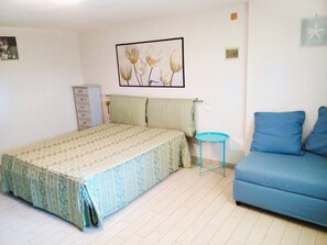 A bedroom with a bed, a blue sofa, a small table, and a wall-mounted picture. - Vacation house Audrey, three-room apartment in detached house with garden (Porto Azzurro)