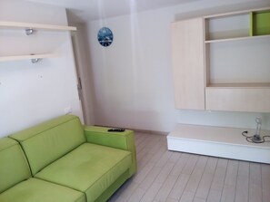 Une pièce avec un canapé vert, un meuble blanc et une horloge murale.