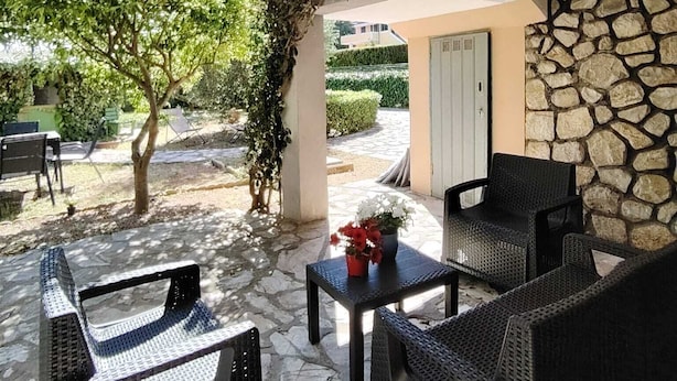 An outdoor patio with wicker furniture, a stone wall, and a view of a garden. - Casa Vacanze Audrey - Porto Azzurro (Porto Azzurro)