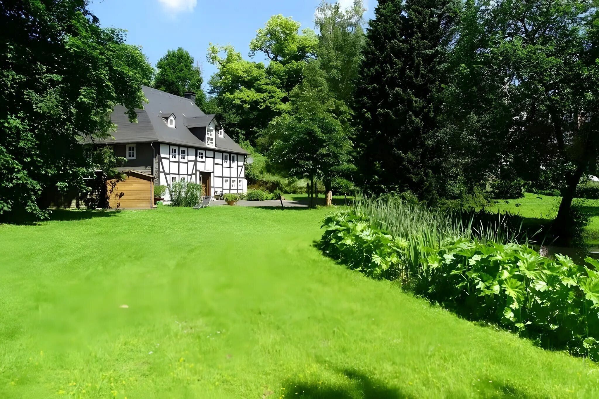 Une maison traditionnelle à colombages, dotée d’une pelouse bien entretenue et de grands arbres.