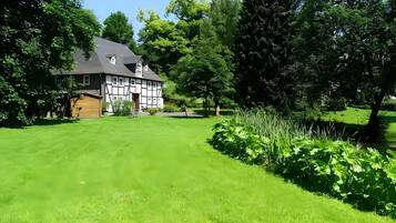 Une maison traditionnelle à colombages, dotée d’une pelouse bien entretenue et de grands arbres.