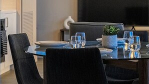 Et moderne spiseområde med et bord dækket til fire personer, en sort sofa og et stort vindue med udsigt over bybilledet.