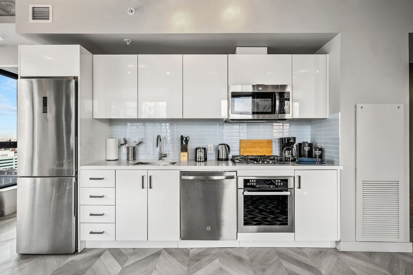 A modern kitchen with stainless steel appliances, white cabinetry, and a herringbone-patterned floor.