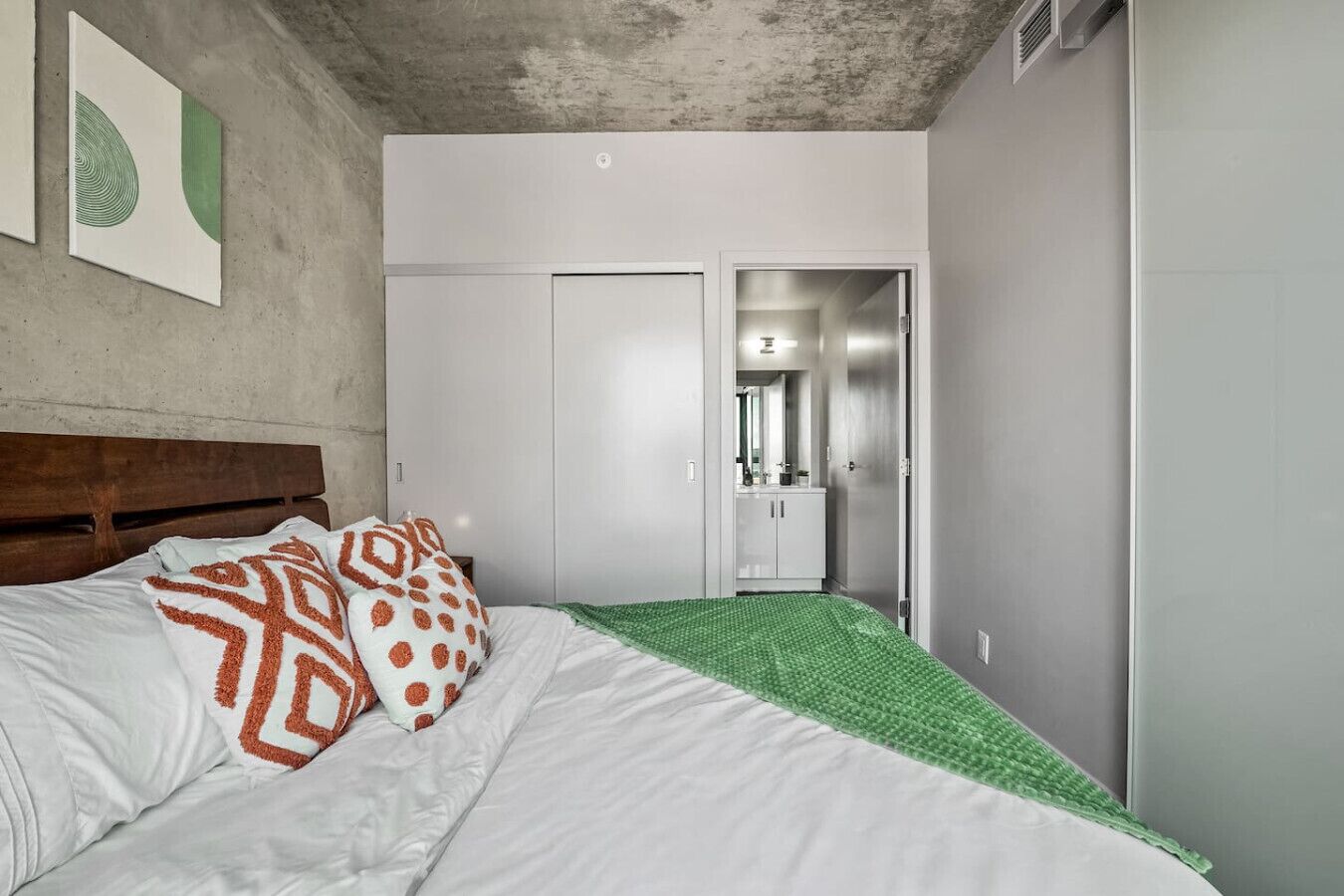 Ein Schlafzimmer mit Bett, Kissen, einem Kleiderschrank und einem durchgegangenen Tür sichtbar liegenden Badezimmer.