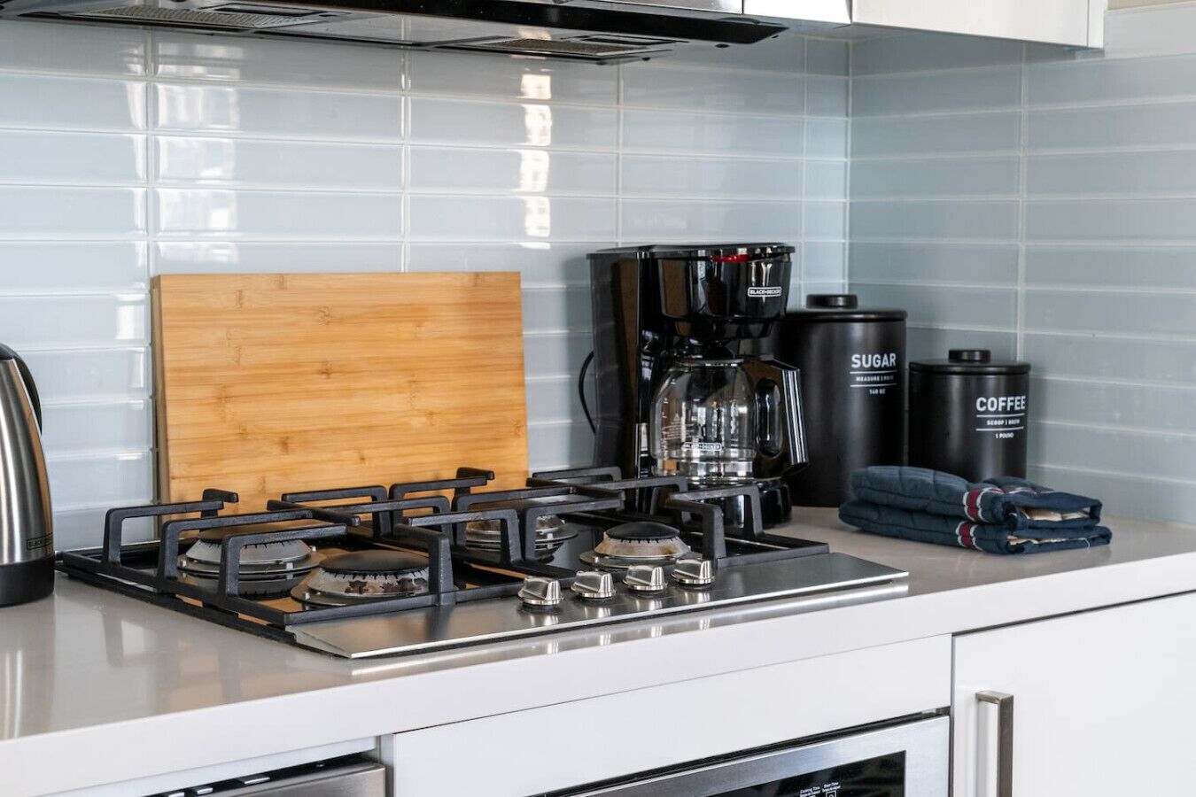 Une cuisine équipée d’une cuisinière à gaz, d’une machine à café et de récipients de rangement.