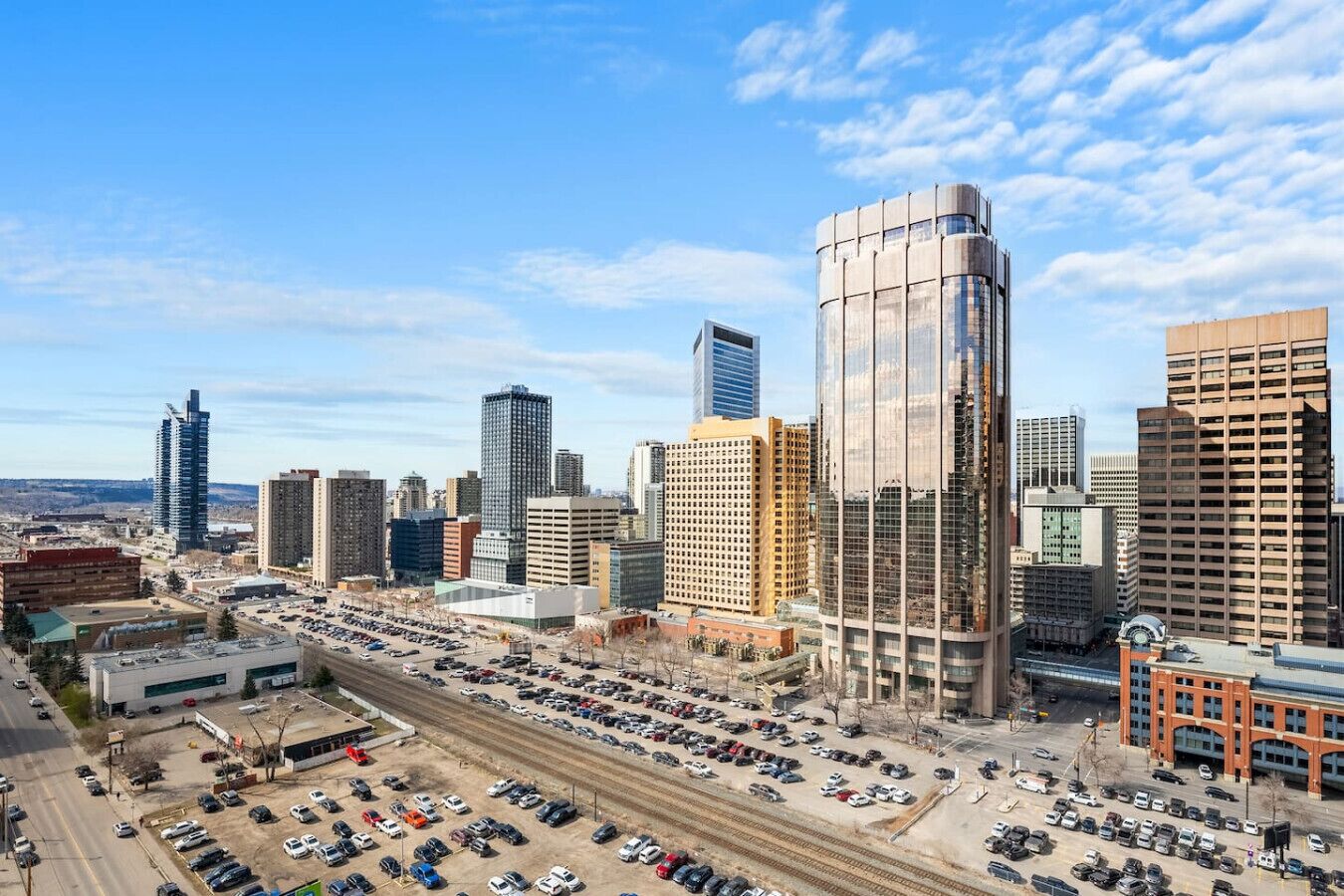A cityscape with modern high-rise buildings, a parking lot, and a railway track.