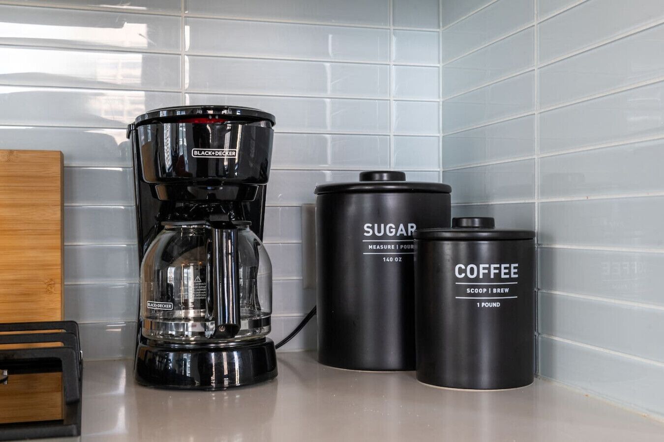 A kitchen counter with a coffee maker, a sugar container, and a coffee container.