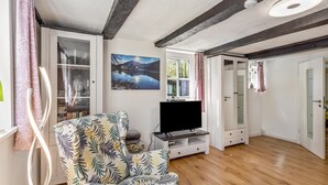 A living room with a wooden floor, a television on a stand, a patterned armchair, a glass cabinet, and a painting of a landscape. - Apartment Kleine Auszeit with Mountain View in Historic Forester’s House (Olsberg)