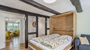 A room with a wooden bed, a grey sofa, and a wooden cabinet. - Apartment Kleine Auszeit with Mountain View in Historic Forester’s House (Olsberg)
