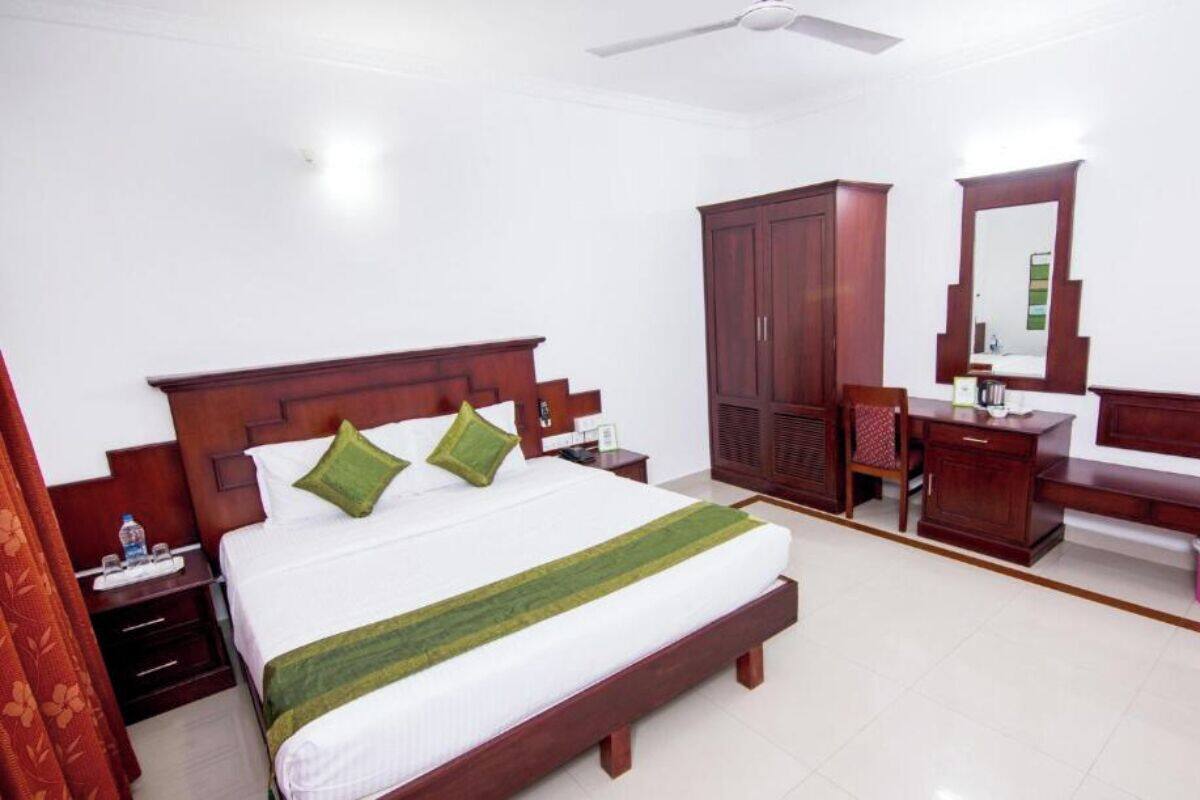 A hotel room with a bed, wooden wardrobe, a vanity with a mirror, and a desk.