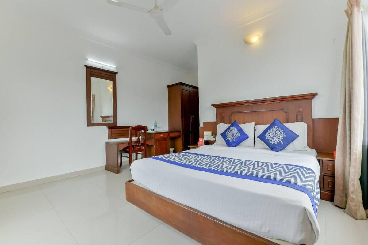 A hotel room with a large bed, a desk, a chair, a wardrobe, and a ceiling fan.