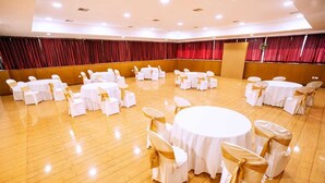 Un salón de banquetes con mesas y sillas redondas, pisos de madera y cortinas rojas.