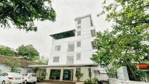 Un edificio de varios pisos con techo plano, un acceso cubierto y un área de estacionamiento con automóviles.