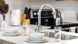 A modern kitchen with a stainless steel sink, white countertops, and a kettle. - Luxe Downtown Haven W / 2 Free Parking! (Calgary)