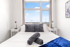 A hotel room with a bed, two bedside tables, a window with a view, and a painting on the wall.