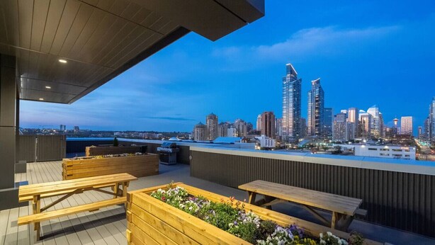 A rooftop terrace with wooden benches and planters, overlooking a city skyline with modern buildings. - Luxe Downtown Haven W / 2 Free Parking! (Calgary)