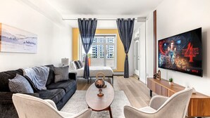 A modern hotel room with a sofa, armchairs, a small table, a TV, and a bed. - Luxe Downtown Haven W / 2 Free Parking! (Calgary)