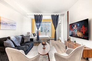 A modern hotel room with a sofa, armchairs, a small table, a TV, and a bed.
