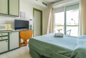 Ein Hotelzimmer mit Bett, Schreibtisch mit Fernseher, kleinem Tisch mit Pflanze und Balkon mit Stuhl.
