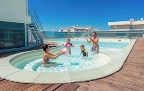 A swimming pool area with a wooden deck, a glass enclosure, and a clear blue sky. - Residence Hotel Club House (Cattolica)